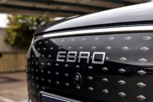 Le grand SUV EBRO en mouvement dans un environnement urbain, avec un indicateur de batterie visible sur le tableau de bord montrant le mode de conduite électrique en action.