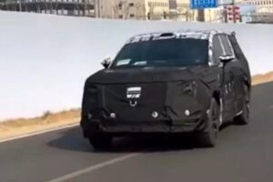 Prototype camouflé d'un grand SUV avec silhouette distinctive et logos Xiaomi partiellement visibles, photographié sur un circuit d'essai fermé avec équipement de test apparent.