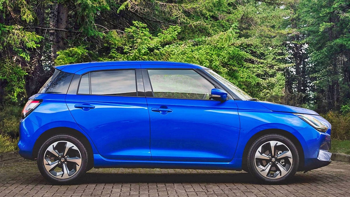 Suzuki Swift 2024 vue de profil en finition de base sur route urbaine, avec jantes tôlées 15 pouces
